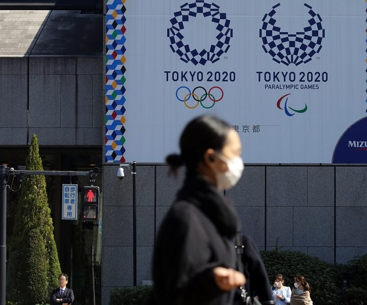 마스크를 쓴 여성이 9일 오후 도쿄 올림픽·패럴림픽 홍보물이 설치된 일본 도쿄도(東京都) 지요다(千代田)구의 한 사거리를 지나는 가운데 근처 신호등에 적신호가 켜져 있다. [사진=연합뉴스]