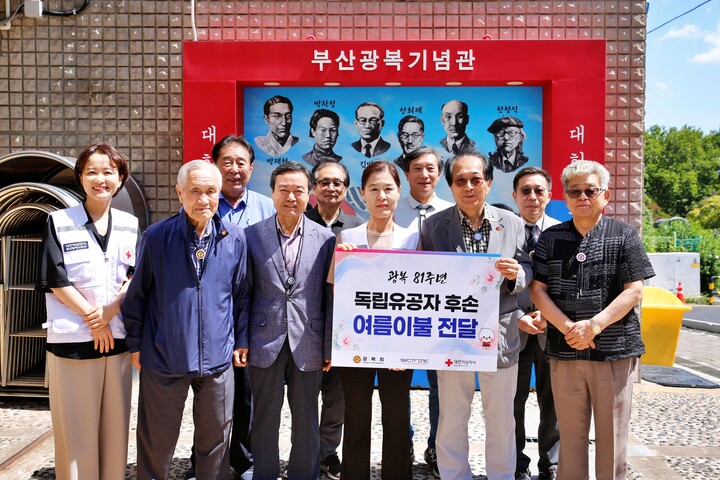 광복 81주년을 맞아 독립유공자 후손에 여름이불을 전달하고 기념사진을 촬영하고 있다.(전달판 좌_앞줄 왼쪽에서 4번째: 대한적십자사 부산지사 박선영 사무처장) [사진=대한적십자사부산지사]